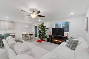 Living room with recessed lighting, ceiling fan, wood finished floors, a glass covered fireplace, and a chandelier