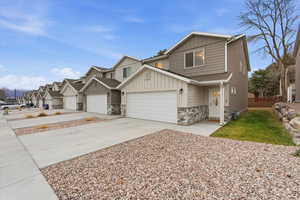 View of front facade featuring board and batten siding, stone siding, concrete driveway, and a garage