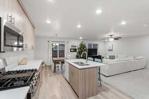 Kitchen with appliances with stainless steel finishes, decorative light fixtures, light wood finished floors, an island with sink, and recessed lighting