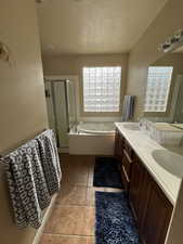 Bathroom with double vanity, a whirlpool tub, a shower stall, light tile patterned floors, and a textured ceiling