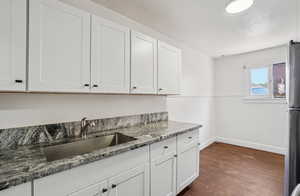 Kitchen with white cabinets, dark stone counters, dark wood-type flooring, and freestanding refrigerator