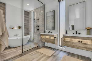 Full bath with walk in shower, a freestanding bath, two vanities, wood finished floors, and recessed lighting