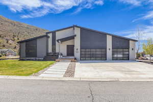 Contemporary home with stucco siding, concrete driveway, covered porch, a garage, and a front lawn