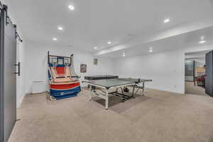 Rec room with a barn door, light colored carpet, and recessed lighting