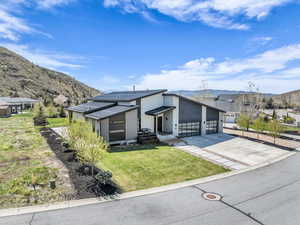 View of front of home featuring a front lawn, a mountain view, roof mounted solar panels, and driveway