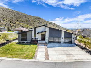 Contemporary home featuring stucco siding, a front yard, driveway, an attached garage, and a mountain view