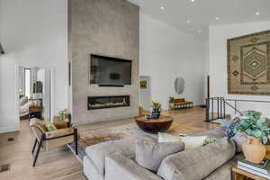 Living area featuring a premium fireplace, a towering ceiling, light wood-type flooring, and recessed lighting