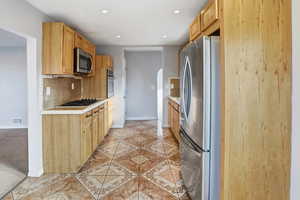 Kitchen featuring stainless steel appliances, light countertops, light tile patterned floors, light brown cabinets, and arched walkways