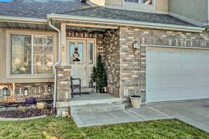 Doorway to property featuring roof with shingles, stone siding, a garage, and stucco siding