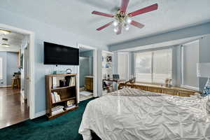 Bedroom featuring a textured ceiling, ensuite bath, ceiling fan, an office area, and dark carpet