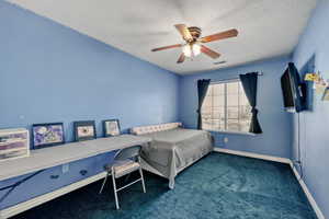 Bedroom with a ceiling fan, dark carpet, and a textured ceiling
