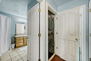 Washroom with stacked washer / drying machine, a textured ceiling, and tile patterned floors