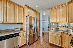 Kitchen featuring appliances with stainless steel finishes, light wood finished floors, a textured ceiling, light brown cabinets, and recessed lighting