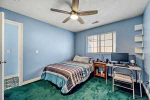 Bedroom with ceiling fan, a textured ceiling, and dark carpet