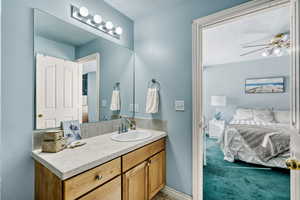 Ensuite bathroom featuring vanity, light colored carpet, and a ceiling fan