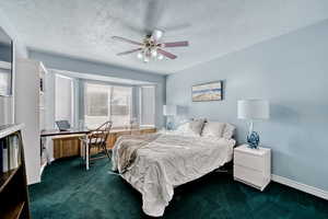 Bedroom featuring dark colored carpet, a textured ceiling, ceiling fan, and a desk