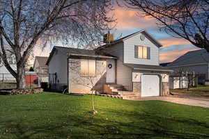 Tri-level home featuring a garage, brick siding, concrete driveway, and a chimney
