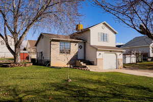 Tri-level home featuring brick siding, a garage, a chimney, and driveway