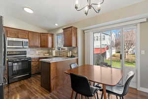 Kitchen with appliances with stainless steel finishes, vaulted ceiling, brown cabinets, backsplash, and dark wood finished floors
