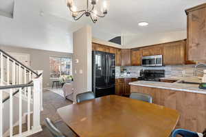 Kitchen featuring black appliances, vaulted ceiling, decorative backsplash, a peninsula, and hanging light fixtures
