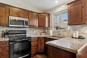 Kitchen featuring black electric range oven, stainless steel microwave, light countertops, tasteful backsplash, and vaulted ceiling