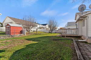 Fenced backyard with a wooden deck, a residential view, and a storage unit