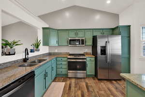 Kitchen featuring stainless steel appliances, green cabinets, light stone counters, dark wood-type flooring, and vaulted ceiling