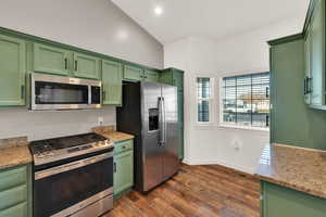 Kitchen with green cabinets, appliances with stainless steel finishes, light stone countertops, and recessed lighting