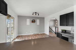Kitchen featuring dark cabinetry, light wood-type flooring, arched walkways, and dark countertops
