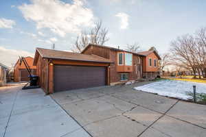 Raised ranch featuring driveway, a garage, roof with shingles, and brick siding