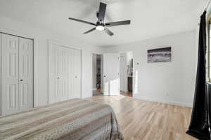 Bedroom featuring two closets, light wood-style flooring, a ceiling fan, ensuite bathroom, and a textured ceiling