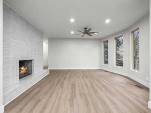 Unfurnished living room with a brick fireplace, light wood-style floors, recessed lighting, and a ceiling fan
