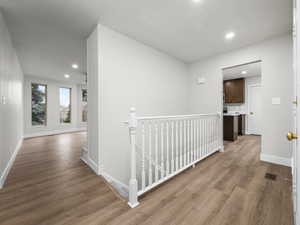 Hallway with an upstairs landing, light wood-type flooring, and recessed lighting