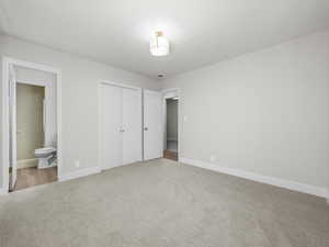 Unfurnished bedroom with ensuite bath, light carpet, and a closet