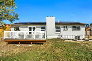 Rear view of house with brick siding, solar panels, a wooden deck, and a lawn