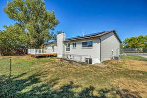 Rear view of property featuring solar panels, a fenced backyard, a wooden deck, and a chimney