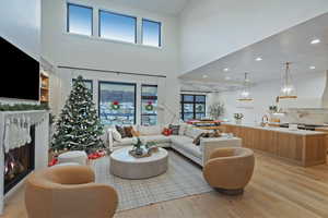 Living area featuring a lit fireplace, light wood-style flooring, a high ceiling, and recessed lighting