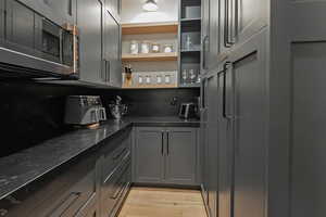 Bar featuring open shelves, dark stone counters, gray cabinetry, and light wood-type flooring