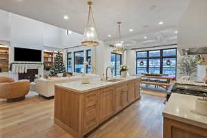 Kitchen featuring light wood-style floors, open floor plan, recessed lighting, light stone counters, and a warm lit fireplace