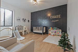 Bedroom featuring an accent wall, a crib, and light wood-style flooring