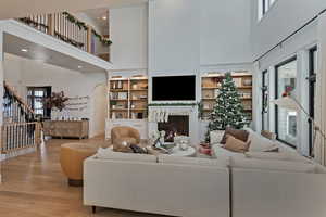 Living room featuring a high ceiling, built in shelves, a warm lit fireplace, wood finished floors, and stairway