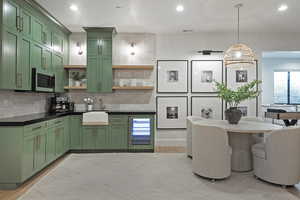 Kitchen featuring green cabinets, beverage cooler, backsplash, stainless steel microwave, and recessed lighting