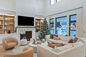Living room featuring a towering ceiling, a lit fireplace, and built in features