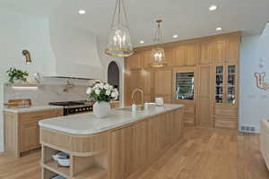 Kitchen featuring open shelves, arched walkways, light wood-style flooring, custom exhaust hood, and recessed lighting