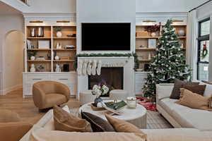 Living area with a lit fireplace, arched walkways, light wood-style floors, and built in features