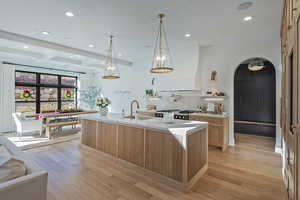 Kitchen with beam ceiling, light wood finished floors, recessed lighting, coffered ceiling, and an island with sink