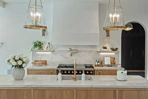 Kitchen with light stone counters, tasteful backsplash, a chandelier, arched walkways, and hanging light fixtures