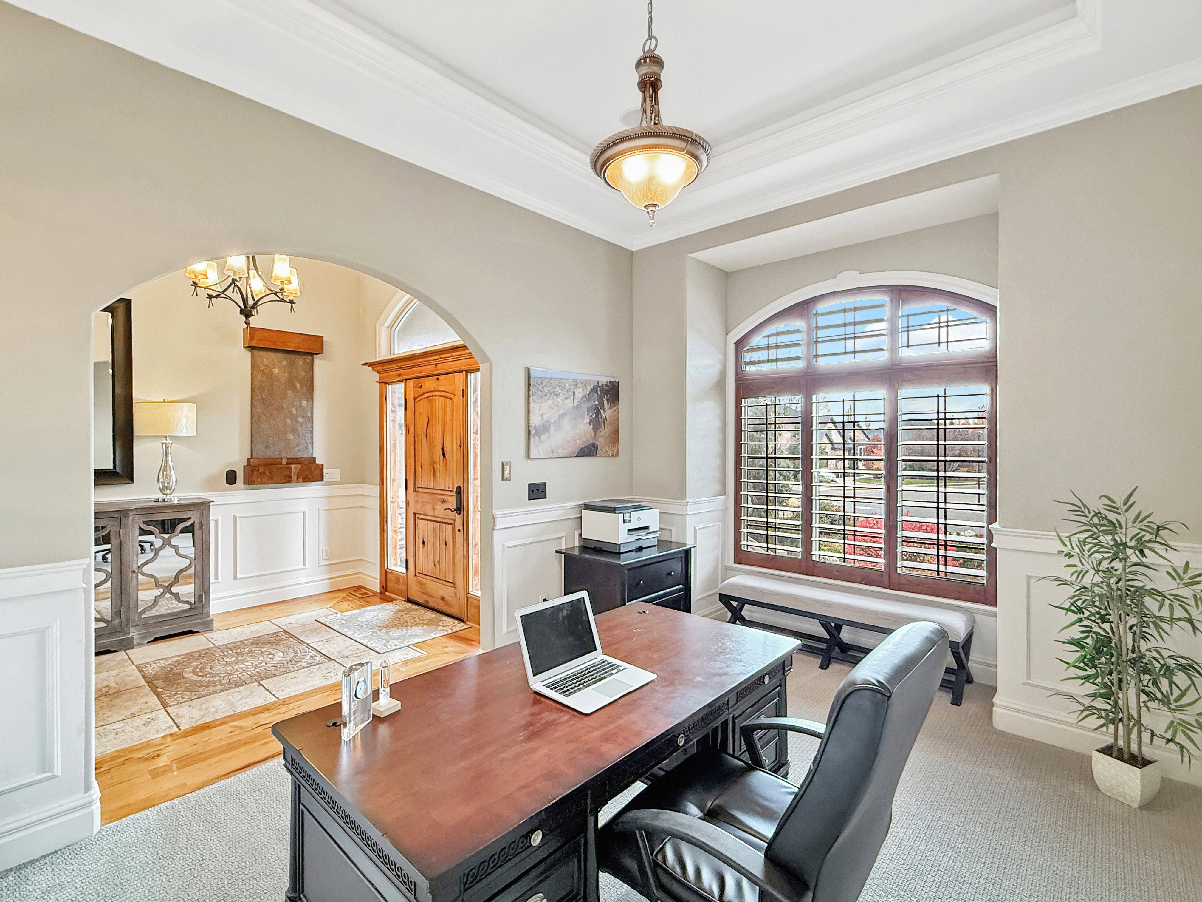 Office space featuring wainscoting, a decorative wall, a chandelier, a raised ceiling, and arched walkways