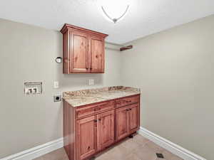 Washroom featuring cabinet space, a textured ceiling, hookup for an electric dryer, washer hookup, and light tile patterned floors