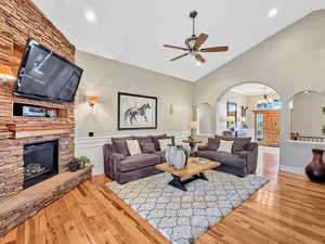 Living area with arched walkways, light wood-style floors, a chandelier, a wainscoted wall, and a fireplace
